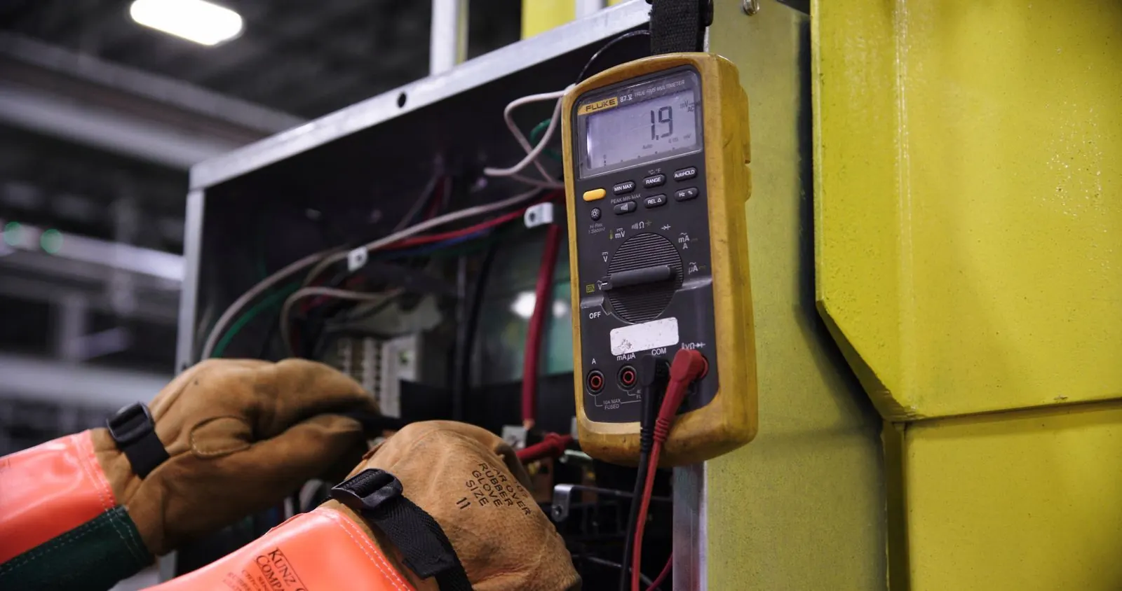 Electricista con guantes dieléctricos mide con un multímetro dentro del tablero de control de una máquina