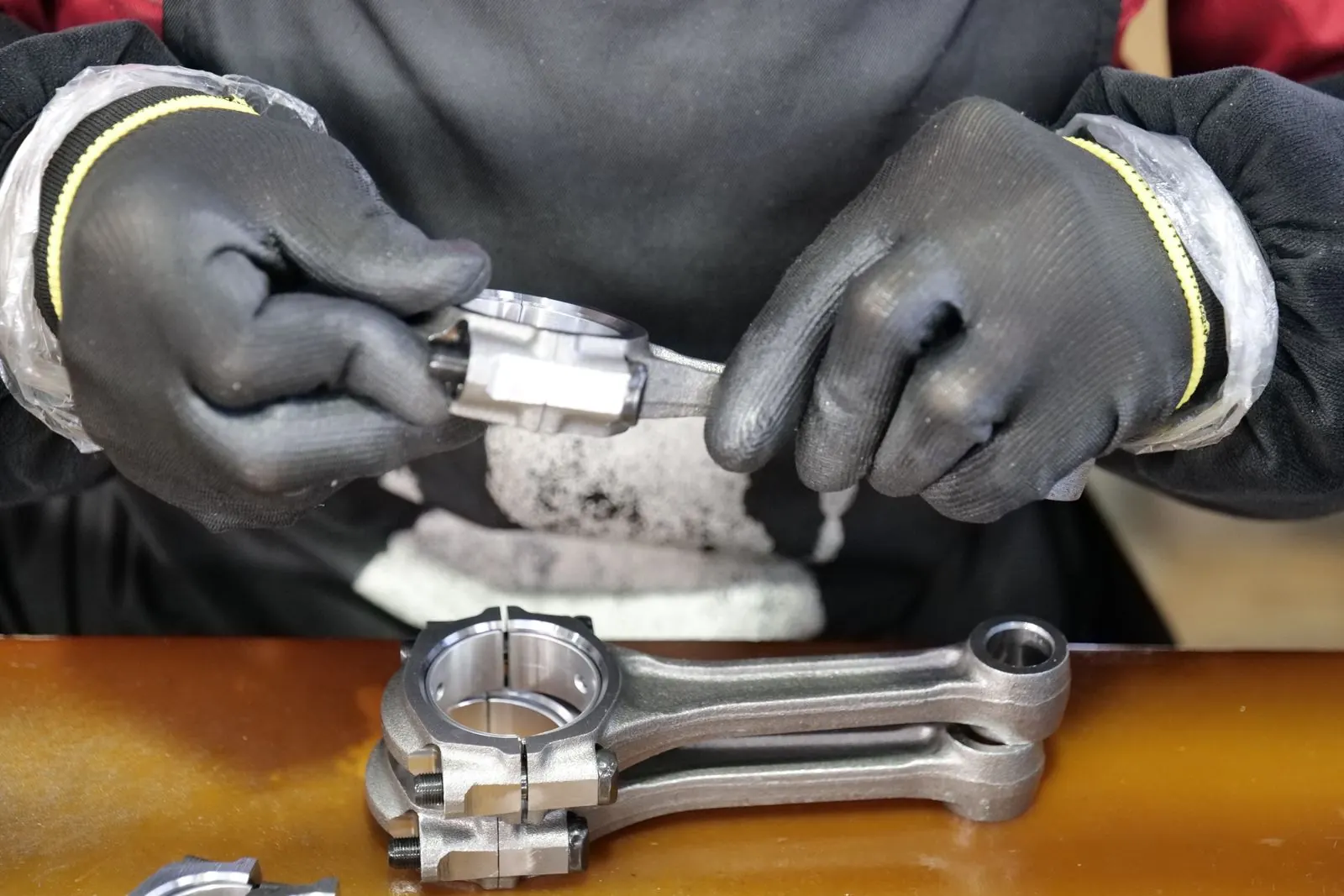 Manos con guantes ensamblan una biela metálica sobre la mesa de trabajo de una línea de ensamble